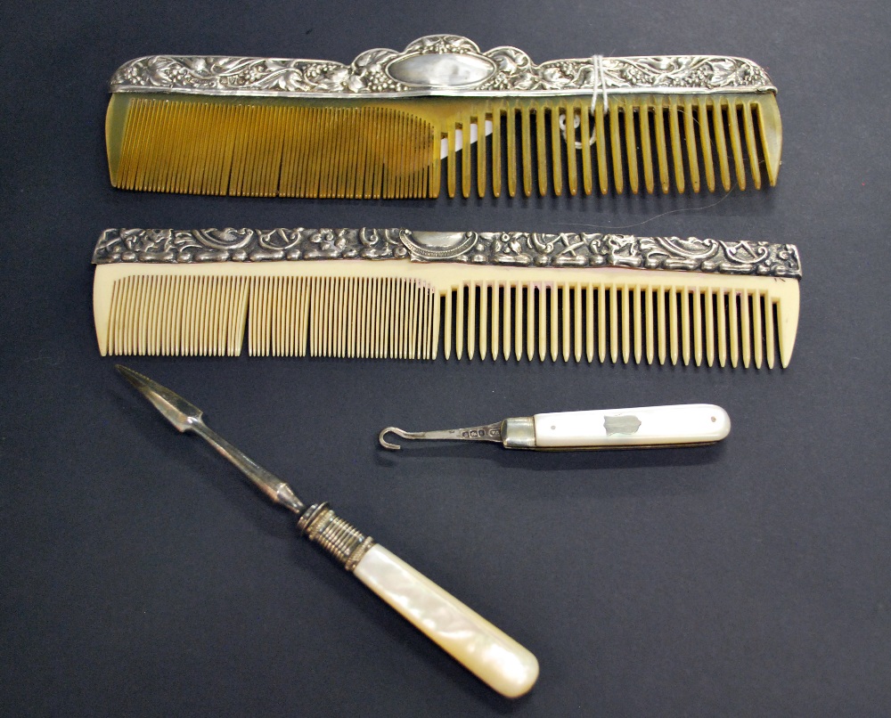 Two silver mounted combs together with a silver and mother of pearl button hook and a cuticle tool.