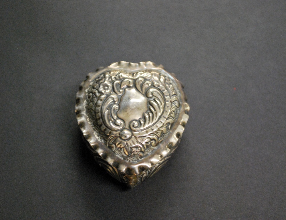 A hallmarked-silver repoussé decorated heart-shaped pill box having a gilt-washed interior.