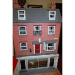 A four storey dolls house in the Victorian style having a protruding twin shop front,