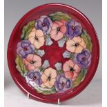 A modern Moorcroft pottery charger, underglaze painted in the Pansy on maroon pattern,