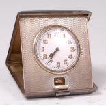 An Art Deco silver cased travel clock/watch, the engine turned case with hinge action,