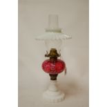 A circa 1900 oil lamp, having a milk glass filled shade above a cranberry glass reservoir,