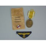 A German Third Reich West Wall Medal in issue packet, together with a Kriegsmarine BeVo cap eagle