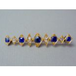 A diamond and sapphire bar brooch, the face composed of nine diamond shaped cells, each centrally