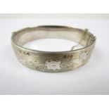 A mid 20th Century silver hinged bangle, the face engraved with a running floral design