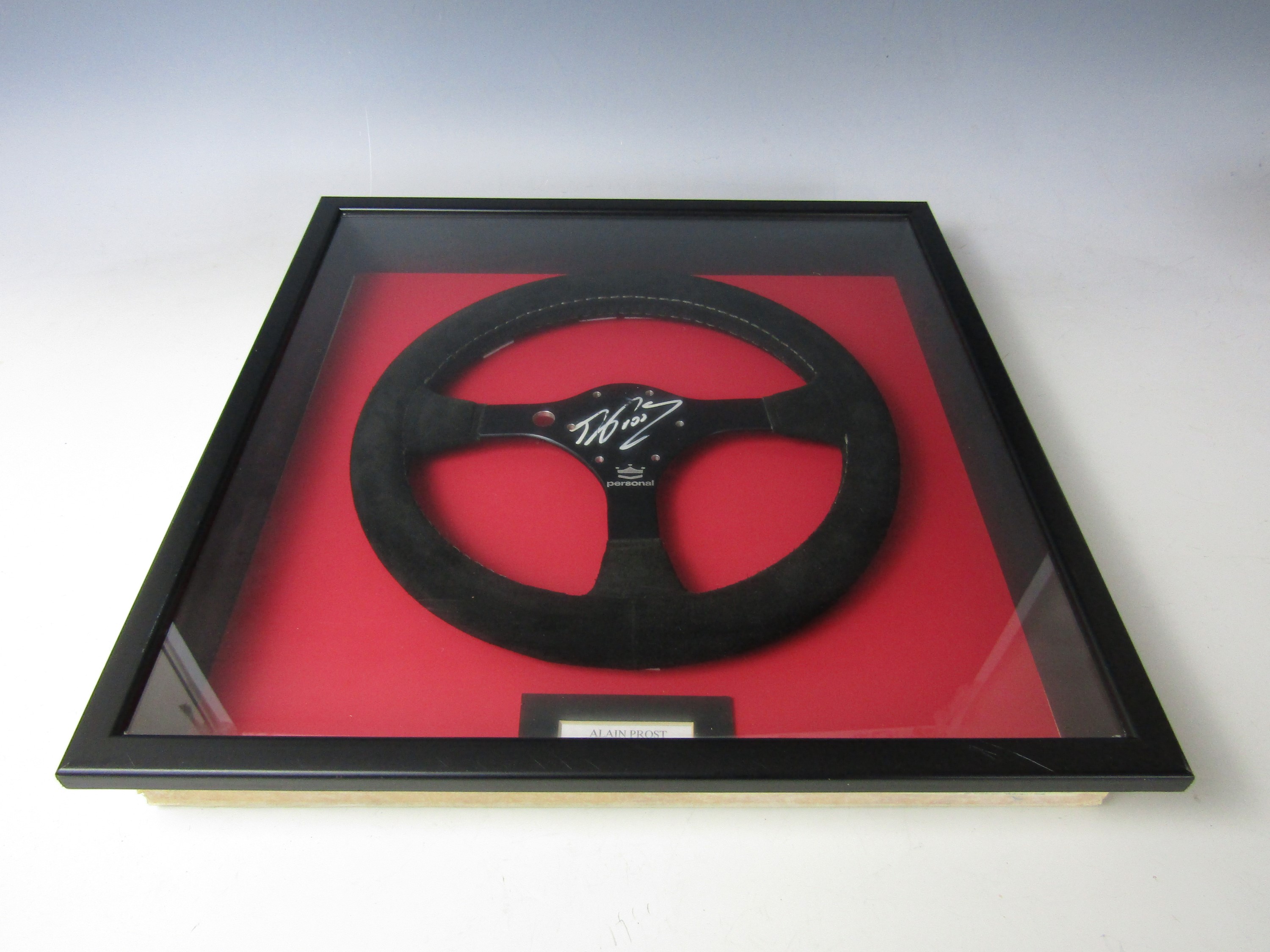 A framed replica Formula 1 steering wheel signed by Alain Prost