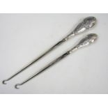 A pair of Edwardian silver handled button hooks, the terminals repousse worked in depiction of