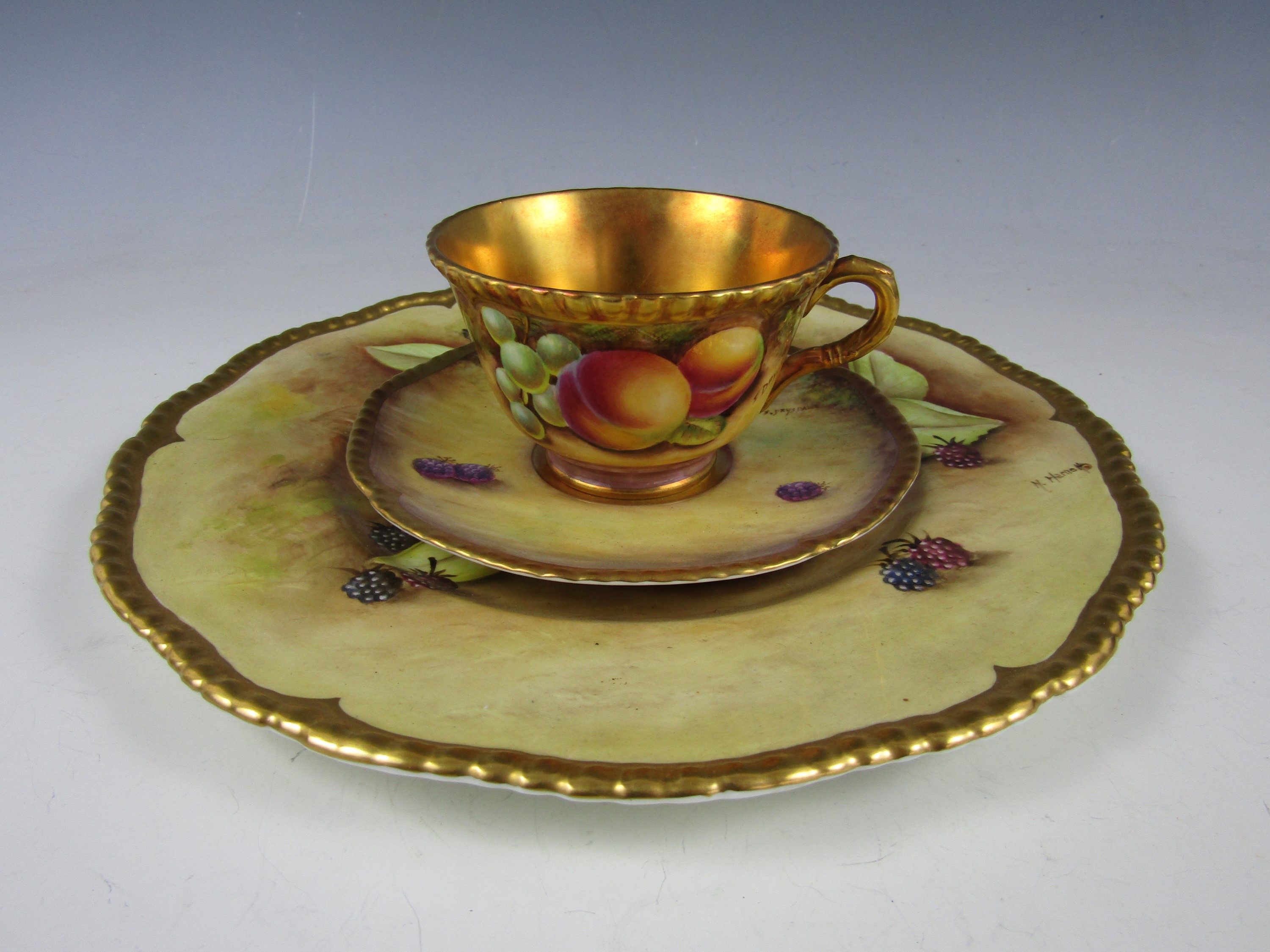 A Coalport bone china trio, each item painted with a fruit still life, comprising tea cup, saucer