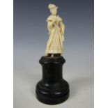 A finely carved ivory statuette of an 18th Century lady with feathered hat, on a turned ebonized