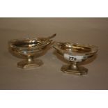 Pair of London silver pedestal salts with clear glass liners and three matching silver spoons,