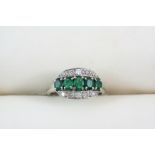 AN EMERALD AND DIAMOND RING centred with five graduated oval-shaped emeralds with old brilliant-