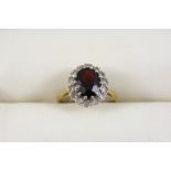 A GARNET AND DIAMOND CLUSTER RING the oval-shaped garnet is set within a surround of single-cut