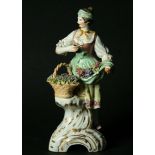 A BERLIN FIGURE OF A FEMALE VINTNER mid-19th Century, standing behind a basket of grapes, blue