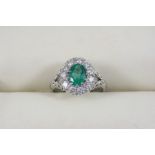 AN EMERALD AND DIAMOND CLUSTER RING the oval-shaped emerald is set within a surround of eleven