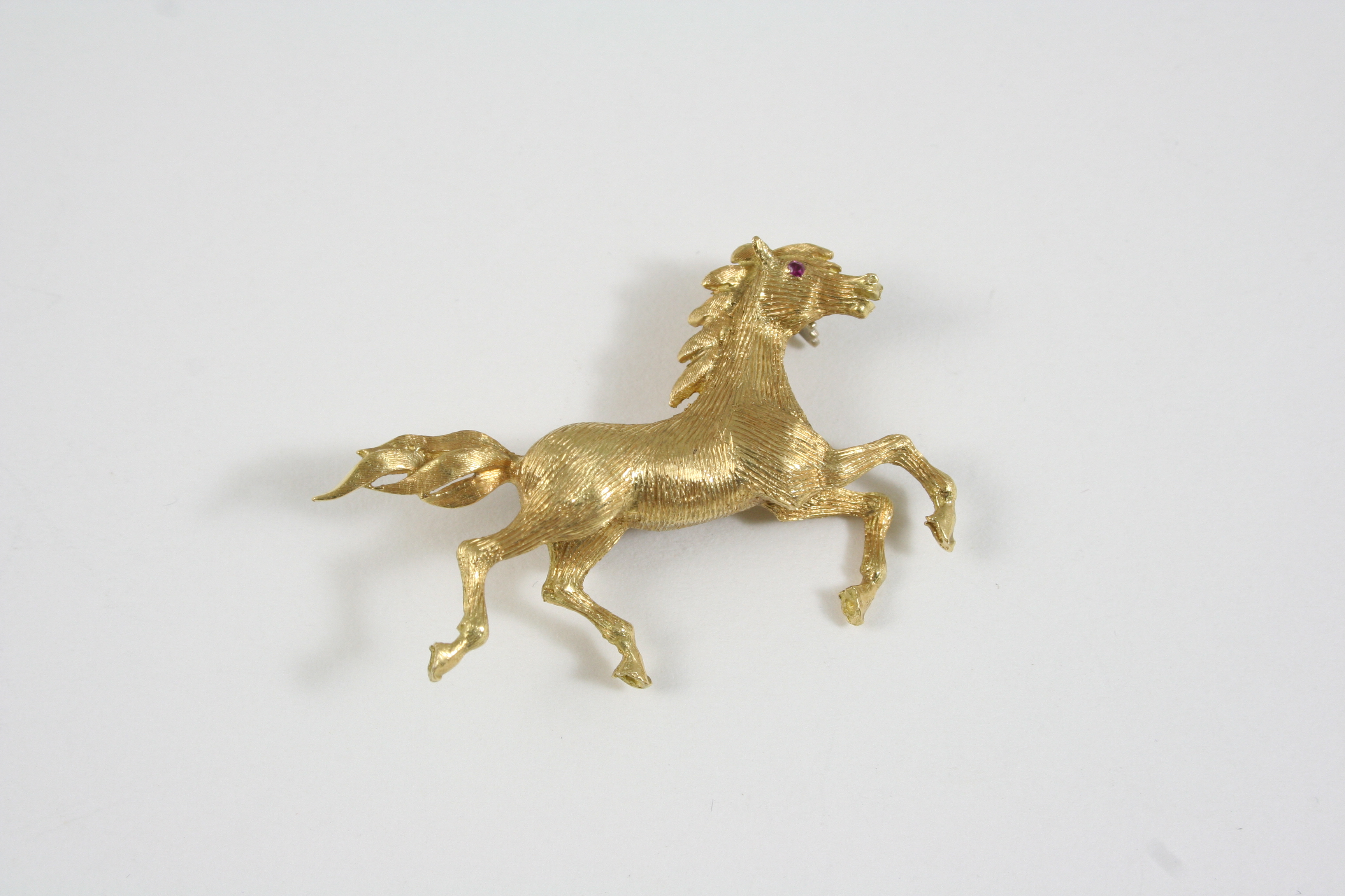 AN 18CT. GOLD HORSE BROOCH realistically formed, with ruby eye, 5cm. wide, 10.8 grams.