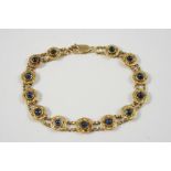 A SAPPHIRE AND GOLD BRACELET formed with graduated engraved circular links each centred with a