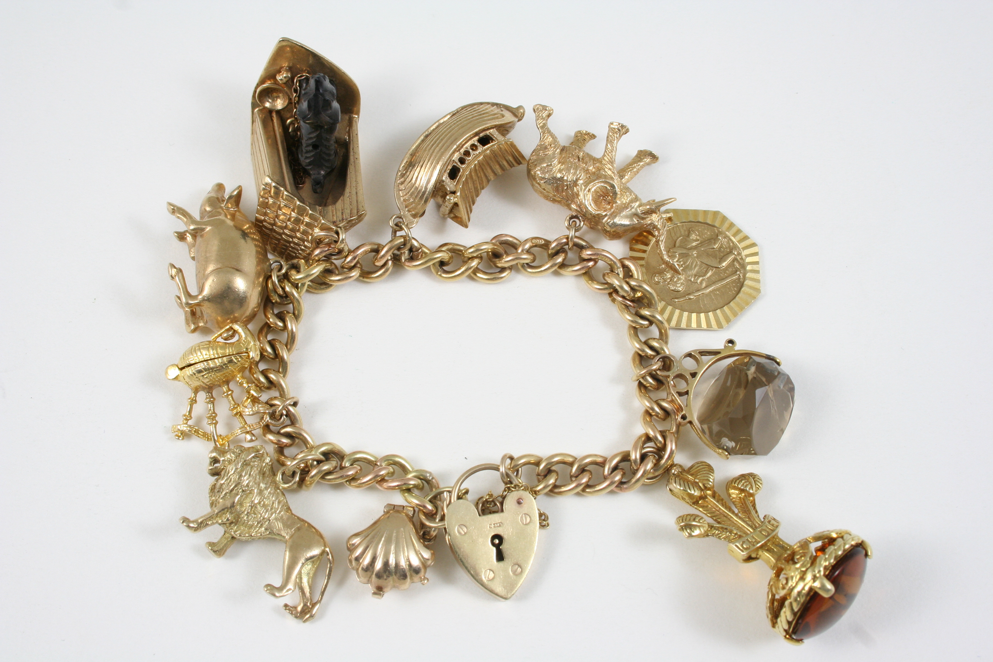 A 9CT. GOLD CURB LINK CHARM BRACELET with padlock clasp, and set with assorted gold charms, 86