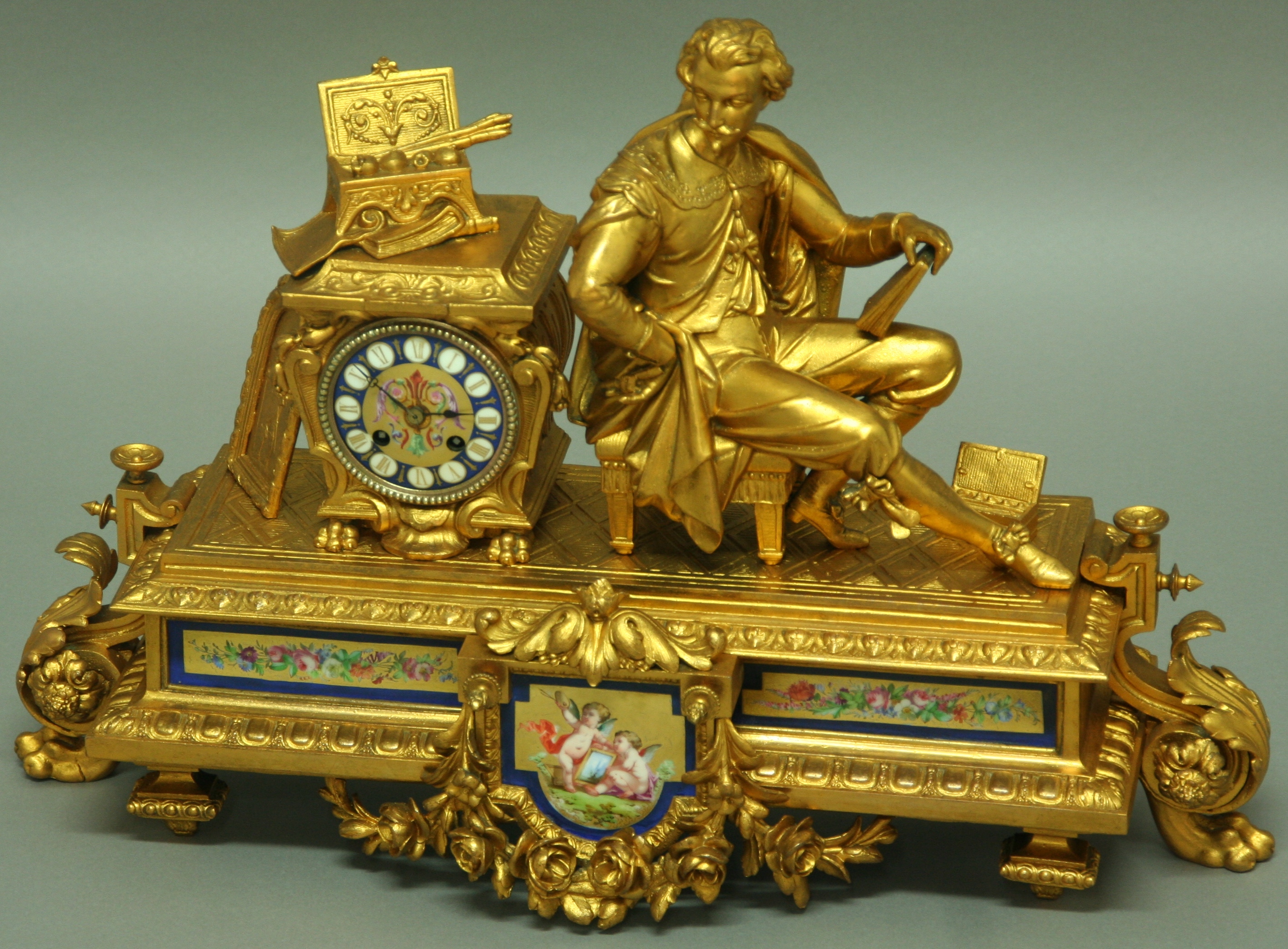 A FRENCH GILT METAL MANTLE CLOCK, late 19th century, a seated figure of an artist beside an urn