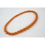 AN AMBER BEAD NECKLACE formed with graduated oval-shaped amber beads, 45.5cm. long, 40 grams.