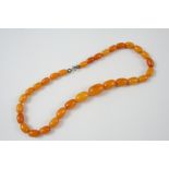 AN AMBER BEAD NECKLACE formed with graduated oval-shaped beads, 40cm. long, 20 grams.