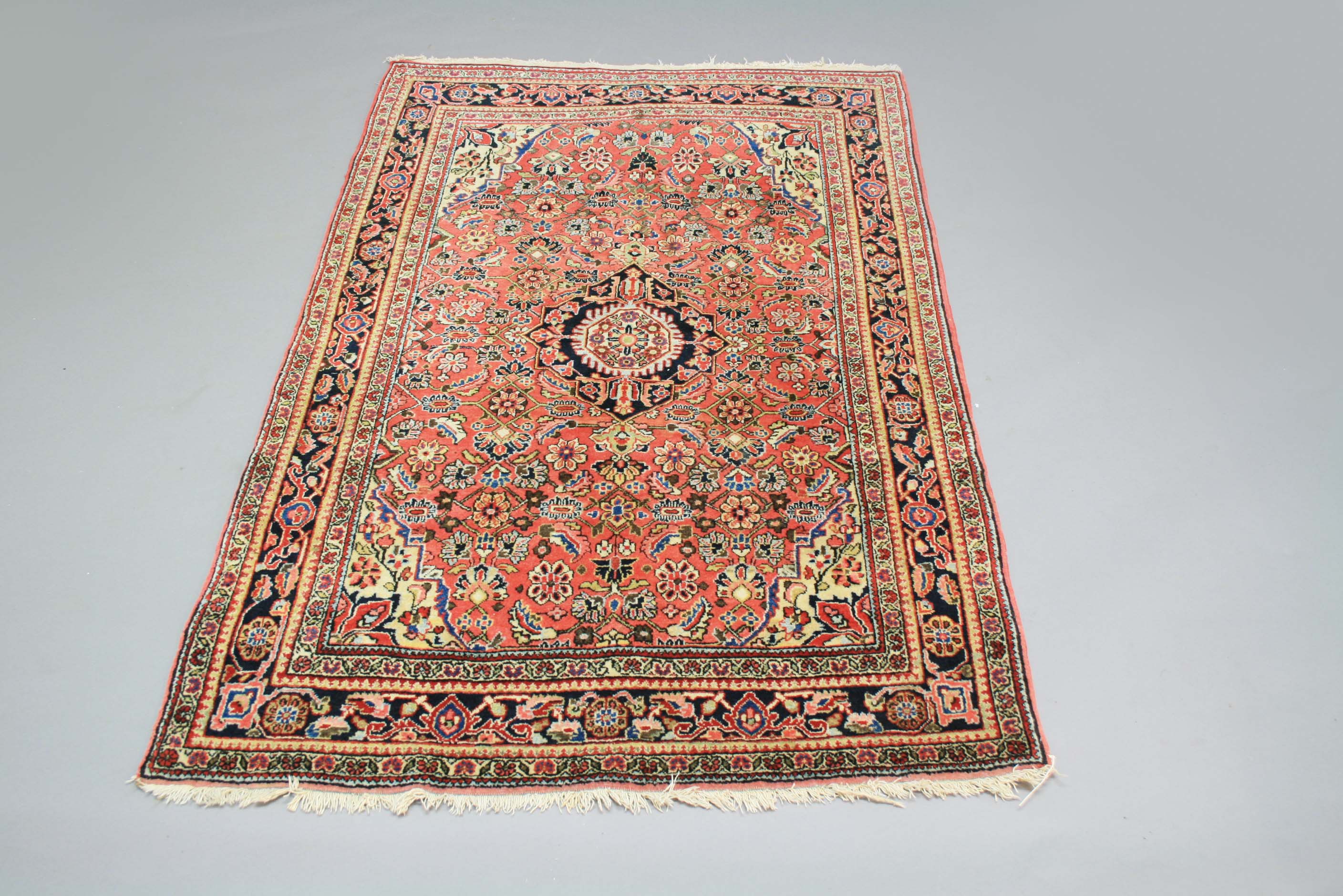 WEST PERSIAN VILLAGE RUG, the coral pink field centred by an indigo medallion surrounded by