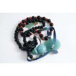 A STRING OF CHINESE MANDARIN BEADS of black glass with red pottery spacers, jade flat plaque and