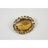 A CITRINE AND GOLD BROOCH set with a large oval-shaped citrine within an ornate gold mount, 5cm.
