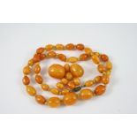 A SINGLE ROW GRADUATED AMBER BEAD NECKLACE 57cm. long, together with some loose amber beads, total