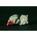 CHINESE GREY JADE DRAGON, recumbent with its head turned, with coral coloured tail and streaks