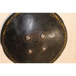 A NATIVE SHIELD. A thick hide 19thC style circular shield with four bosses and decorated obverse,
