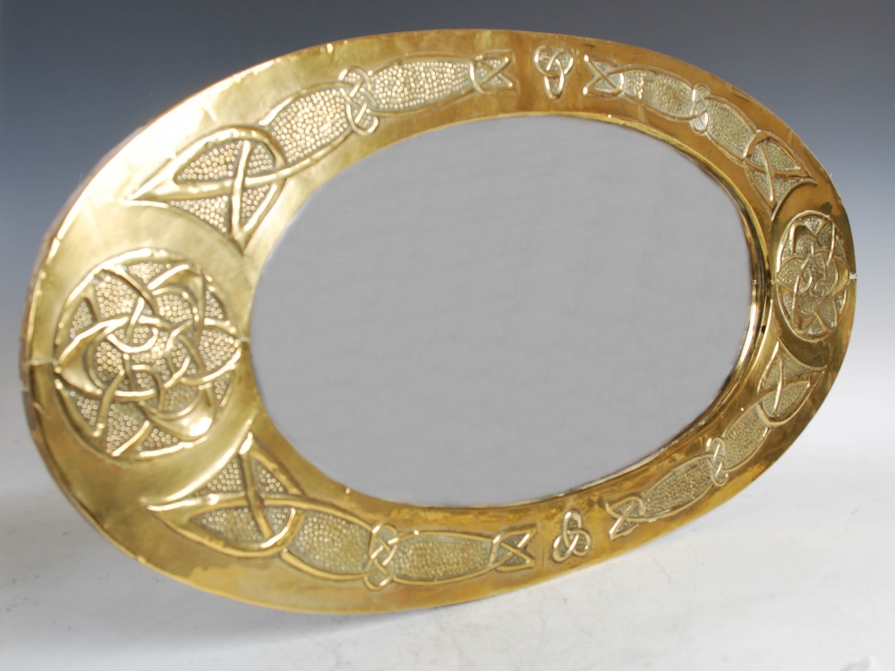 A Scottish Arts & Crafts brass wall mirror, the oval bevelled mirror plate within an embossed Celtic