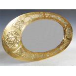 A Scottish Arts & Crafts brass wall mirror, the oval bevelled mirror plate within an embossed Celtic