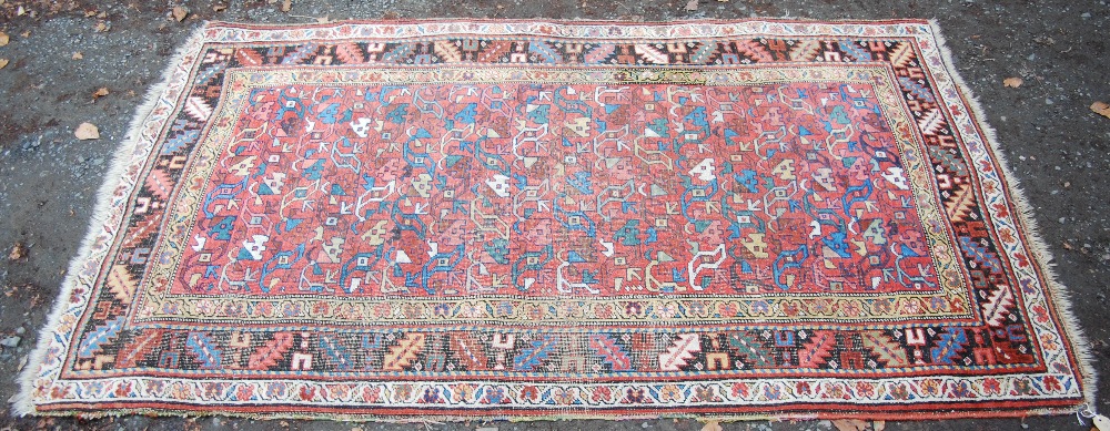 A Persian rug, late 19th/ early 20th century, the madder ground worked in coloured threads with rows