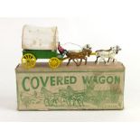 A Wild West-style covered wagon cast metal toy, the green wagon with yellow wheels,