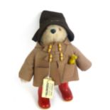 A stuffed Paddington bear in original Dunlop red wellington boots, brown overcoat and luggage label,