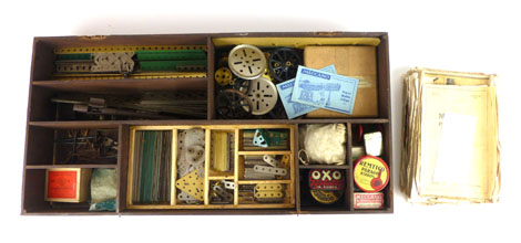 A lift top wooden storage box containing an assortment of various Meccano pieces to include wheels,
