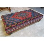 HEARTH STOOL, rectangular shirvan carpet upholstered on turned feet and castors, 120cm x 64cm.