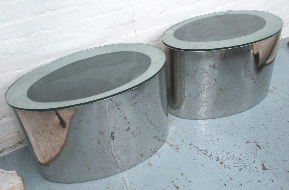 LOW TABLES, a pair, by Megaron, in the form of polished metal ovals with glass top,