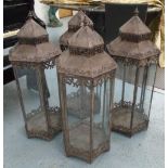 STORM LANTERNS, a set of four, in a distressed metal with glass panels, 95cm x 38cm.