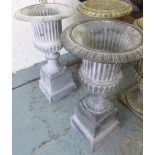 URNS ON PLINTHS, a pair, Classical style, grey cast iron, 101cm H x 54cm diam.