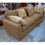 SOFA, in a soft burnt umber fabric on oversized slim black supports and a scatter of cushions,