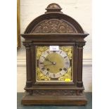 An Edwardian oak mantel clock, the arched top with floral carving over a brass dial with silvered