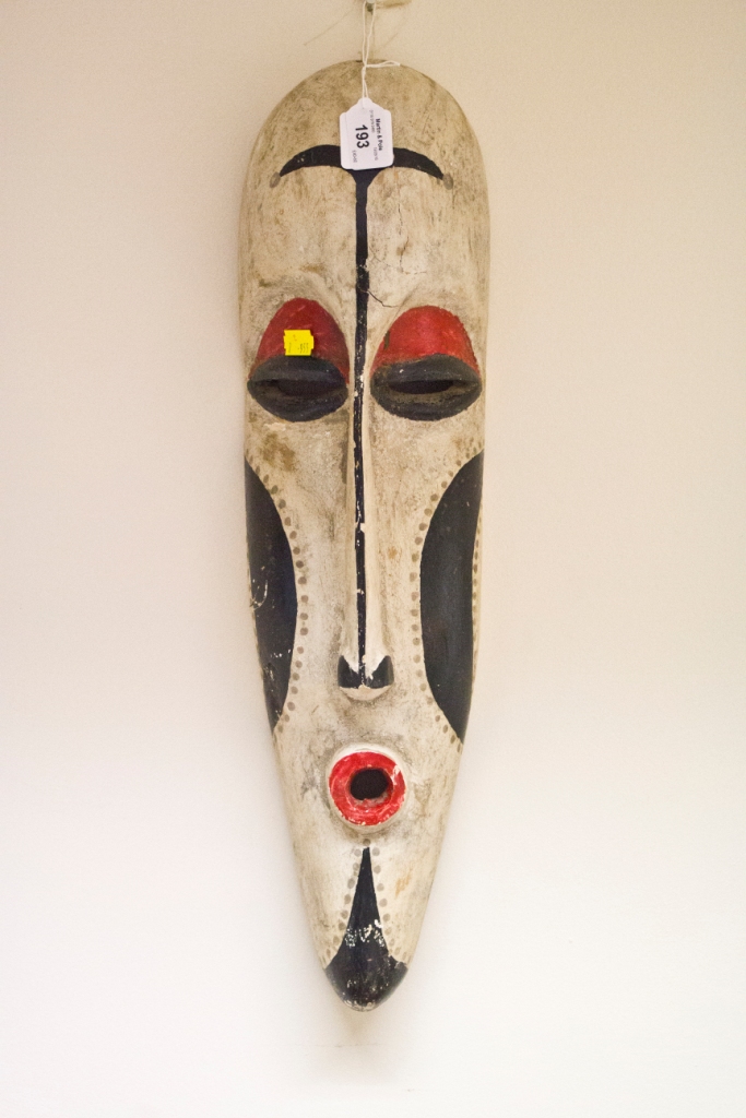 A tribal mask in red, black and white with elongated face, possibly African, 54cm high