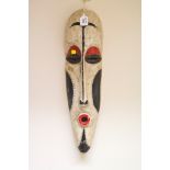 A tribal mask in red, black and white with elongated face, possibly African, 54cm high