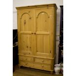 A pine wardrobe, with two doors over two short and one long drawer on turned feet, 135cm wide