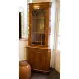 A yewwood veneered corner cabinet, the moulded cornice over a glazed door and panelled cupboard base