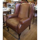 A brown leather wing armchair, on cabriole legs with club feet