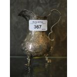 A Victorian silver cream jug with decoration in relief sat on three feet, London 1865