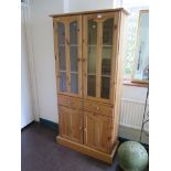 A pine display cabinet, with a pair of glass doors over two drawers and two panelled cupboard