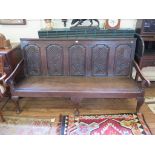 An 18th century oak settle, the lunette carved five panel back over a solid seat and scroll arms